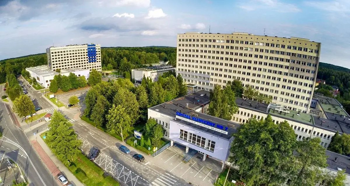 Widok z lotu ptaka na kompleks budynków szpitalnych otoczony zielenią.
