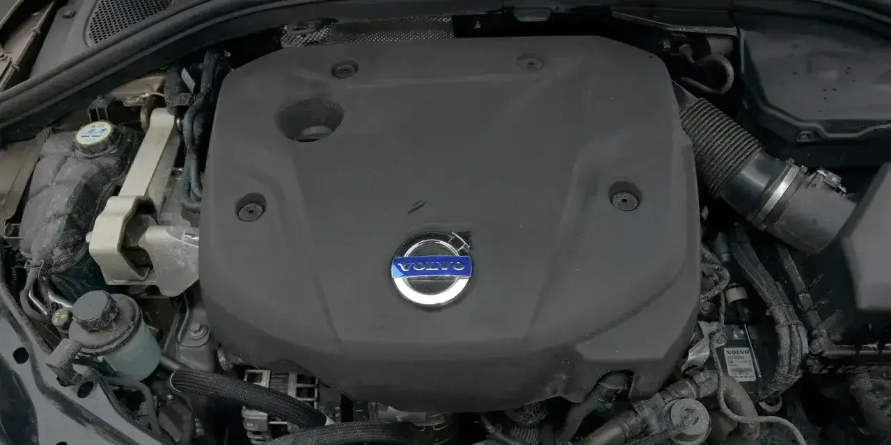 Silnik D4 Volvo pod czarną osłoną z niebieskim logo. Widać fragmenty przewodów i zbiornik płynu.