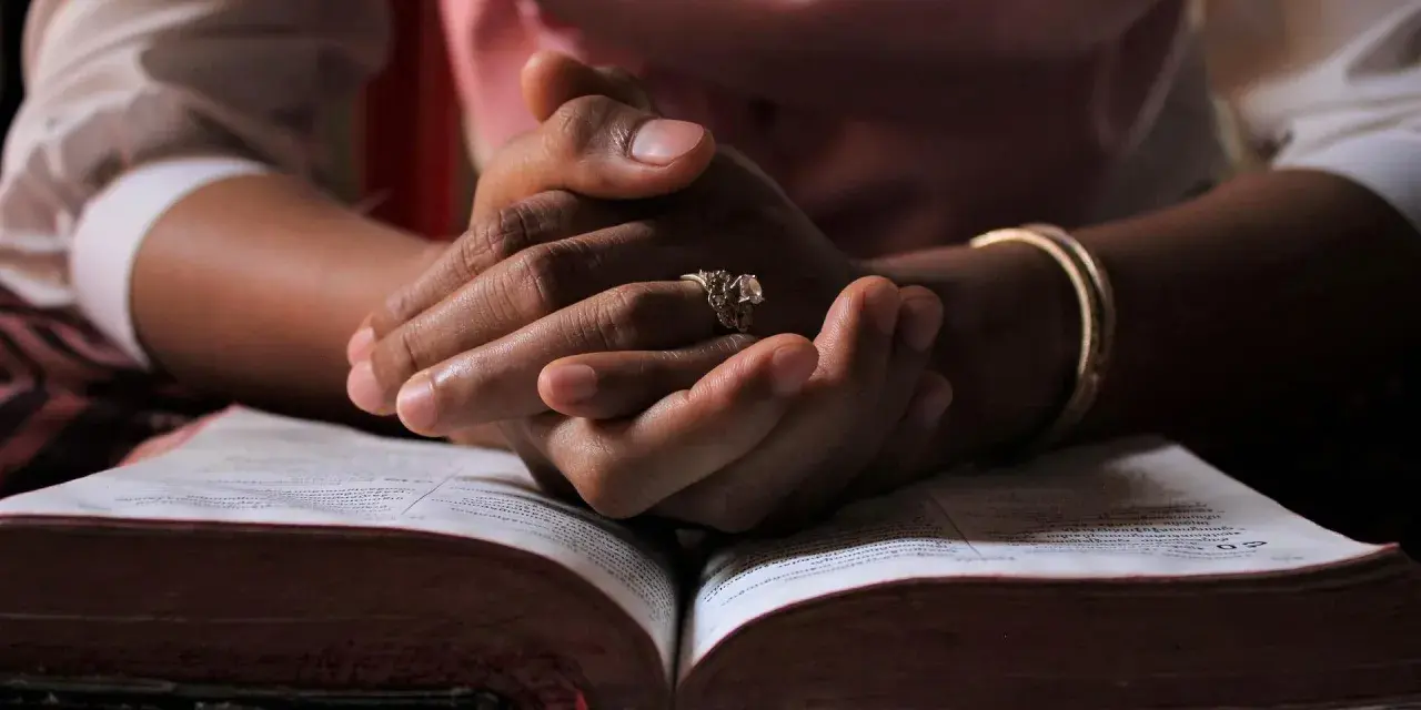 Dłonie z pierścionkiem i bransoletką spoczywają na otwartej Biblii. W ciszy rozbrzmiewa psalm 150.