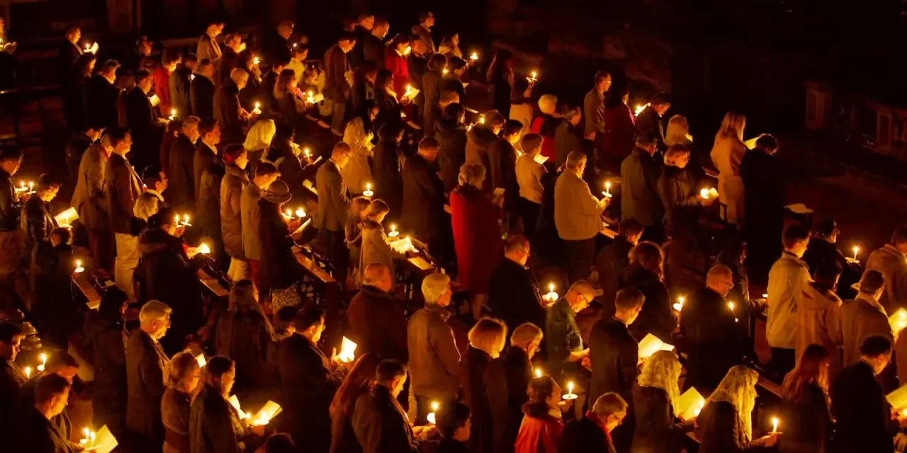 A solemn vigil unfolds as a congregation holds candles, their faces illuminated by the soft glow.
