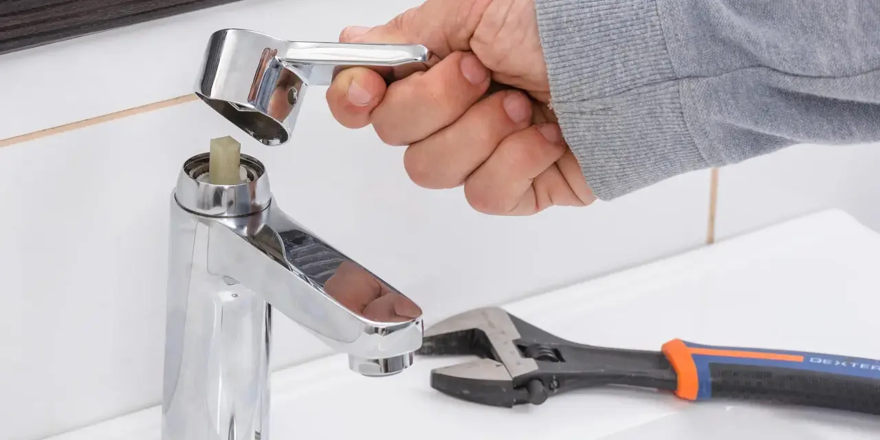 Mano desmontando grifo monomando. Llave inglesa y llave Allen cerca.
