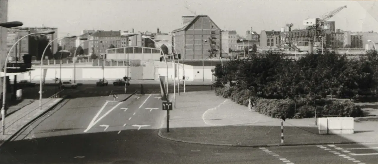 Straßenszene in Berlin der 80er Jahre mit Autos, Ampeln und einem Kran im Hintergrund.