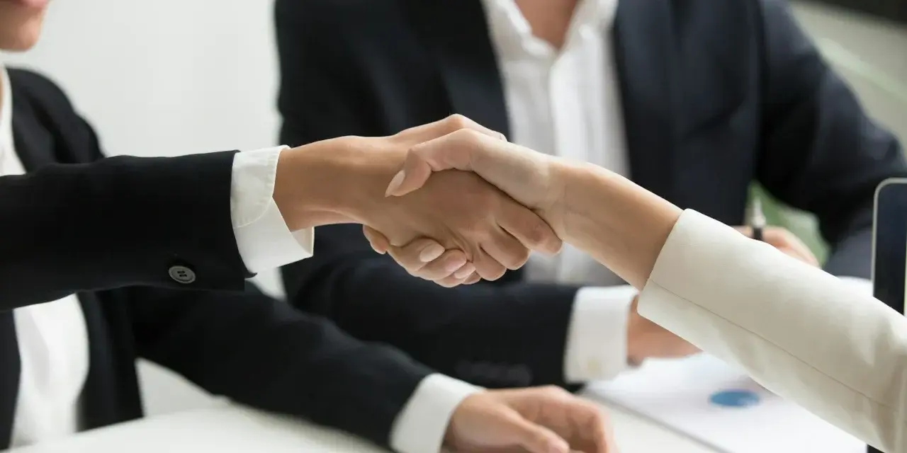 Poignée de main entre deux personnes en costume, symbolisant un accord ou un changement de dirigeant.