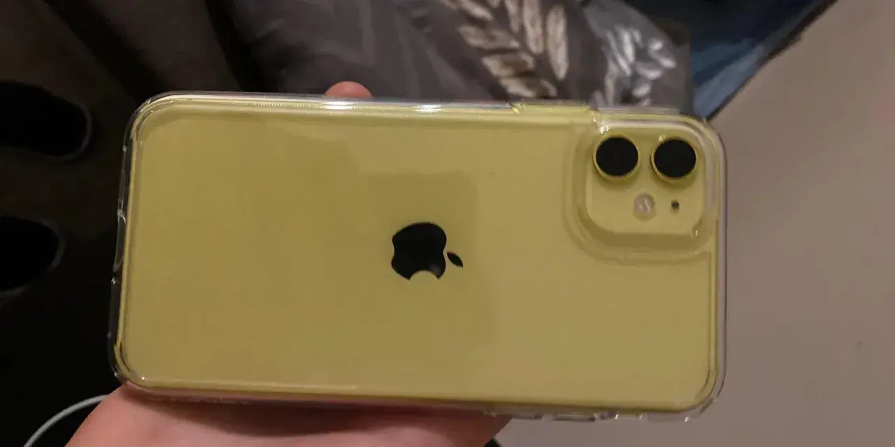 Żółty iPhone 11 w przezroczystym etui, trzymany w dłoni.