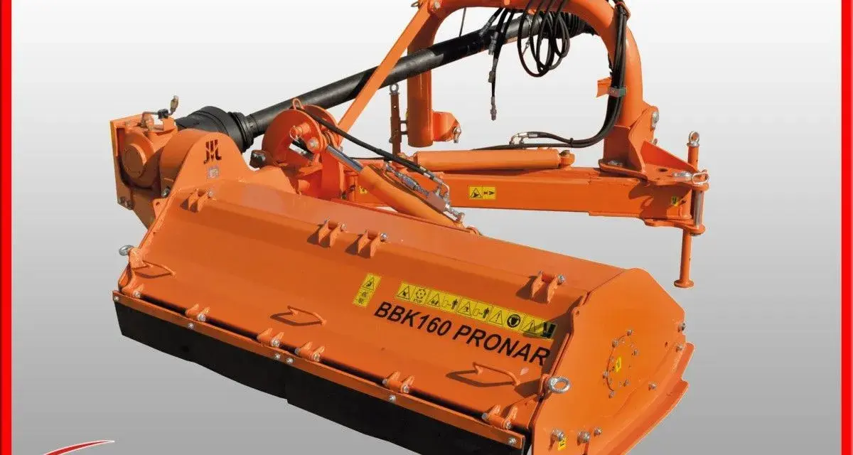 Pomarańczowa kosiarka tylno boczna BBK160 PRONAR z wałkiem WOM i elementami hydraulicznymi, gotowa do pracy w polu.