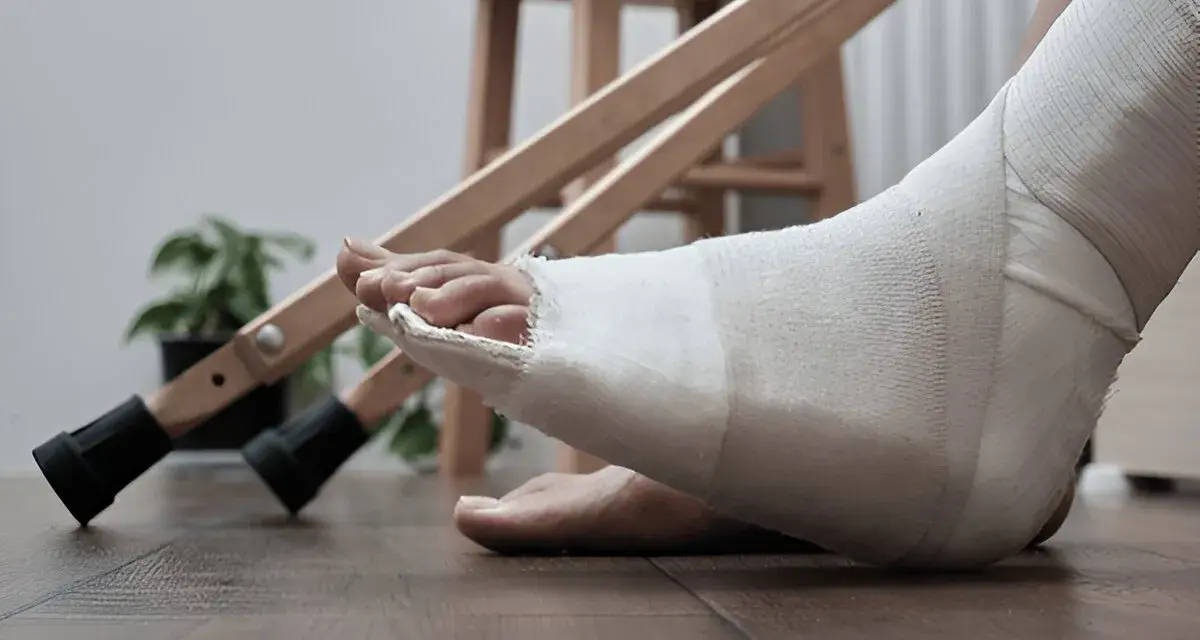 Noga w opatrunku, przygotowanie do rehabilitacji palca po złamaniu. Obok stoją kule.