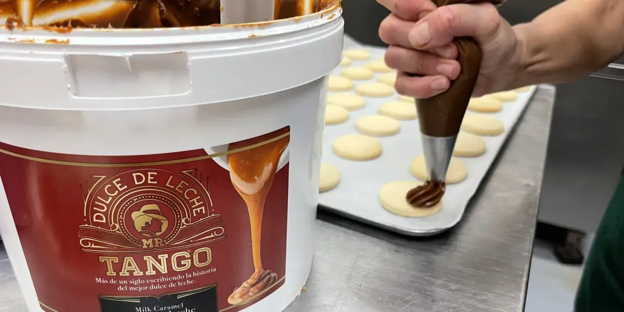 Un repostero usa una manga pastelera para decorar galletas con dulce de leche, mostrando cómo hacer dulce de leche.