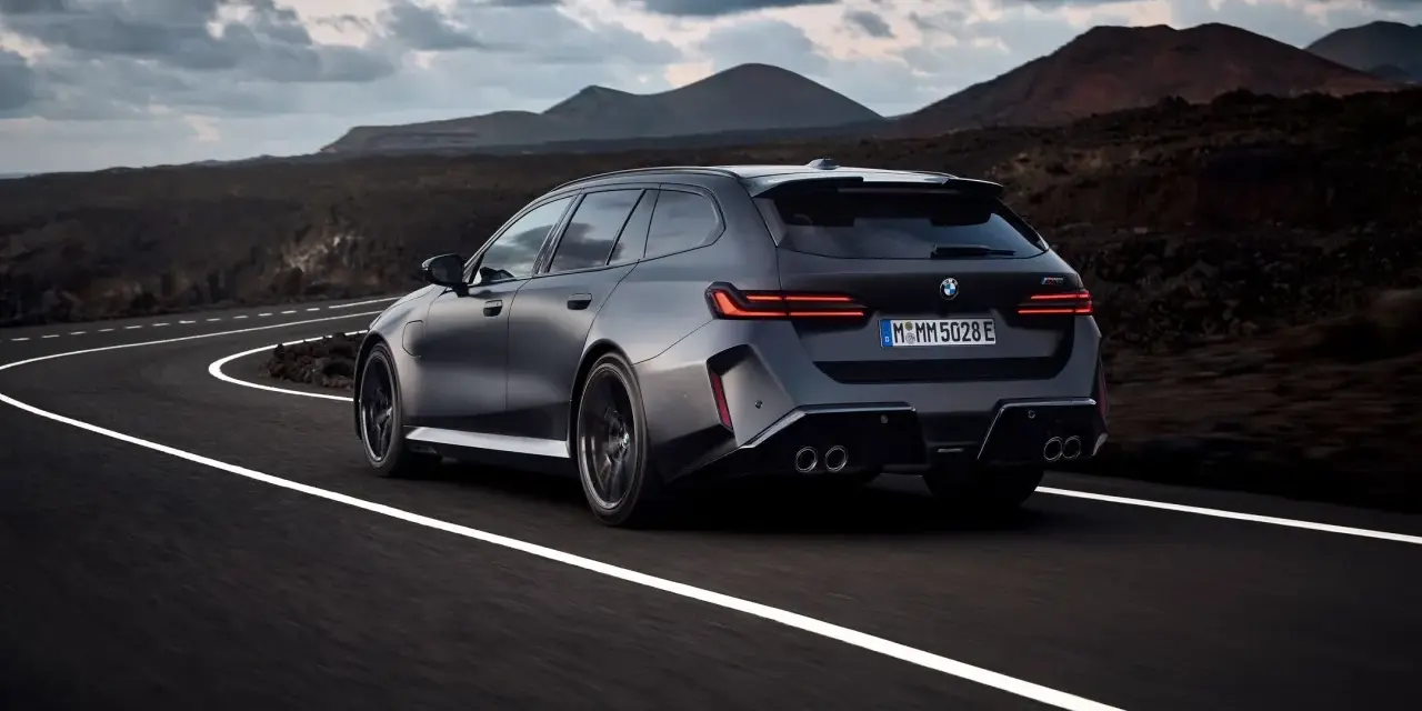 Mocne BMW M5 Touring pędzi po krętej drodze pośród surowego krajobrazu.