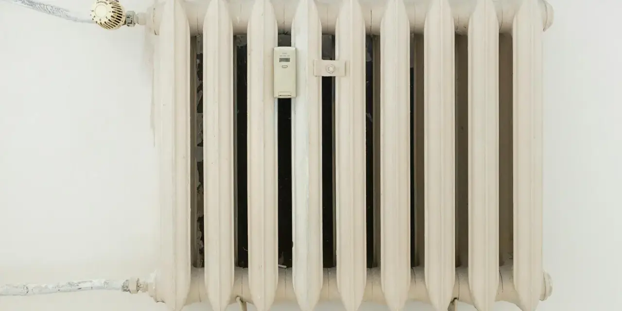Biały grzejnik żeberkowy z termometrem i zaworem. Optymalna temperatura dla taryfy g12.