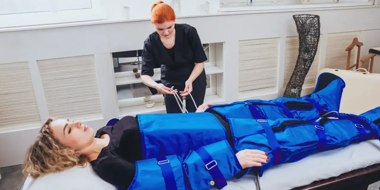 Kobieta w salonie piękności przechodzi zabieg drenażu limfatycznego. Terapeuta przygotowuje urządzenie do masażu uciskowego.