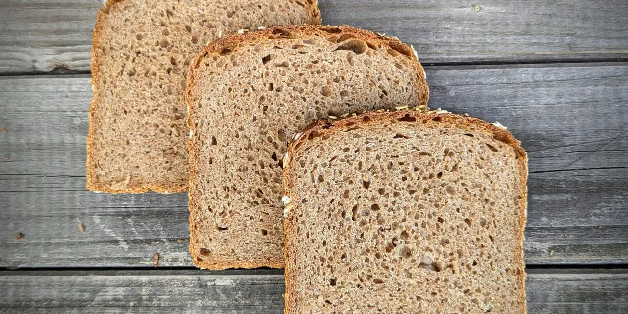 Drei Scheiben **Vollkornbrot** aus der **Kastenform** liegen auf rustikalem Holz.
