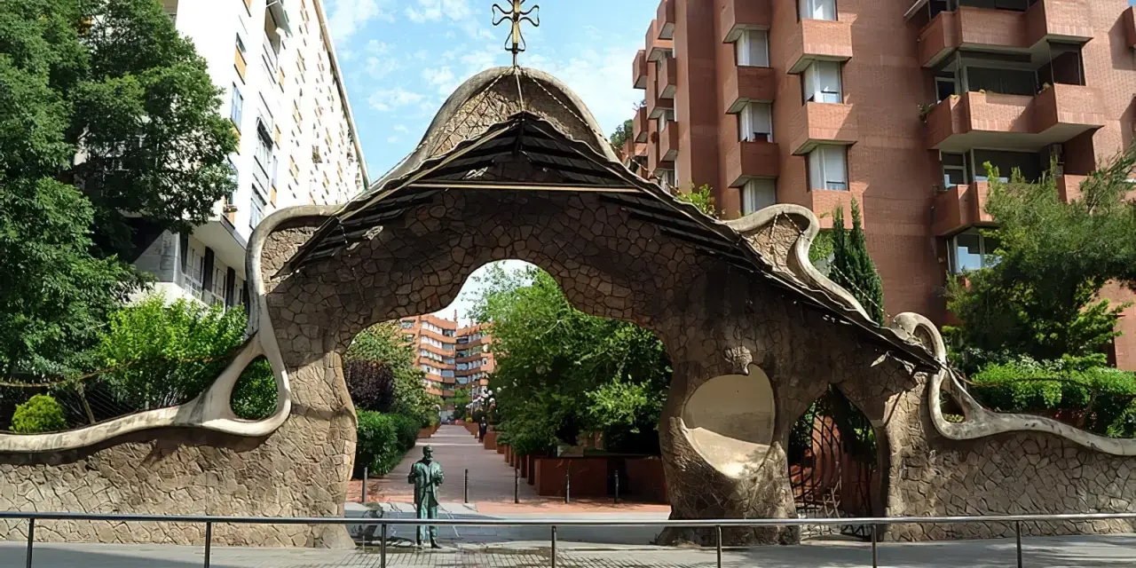 Portail organique, œuvre de Gaudí à Barcelone, avec une statue d'homme devant.
