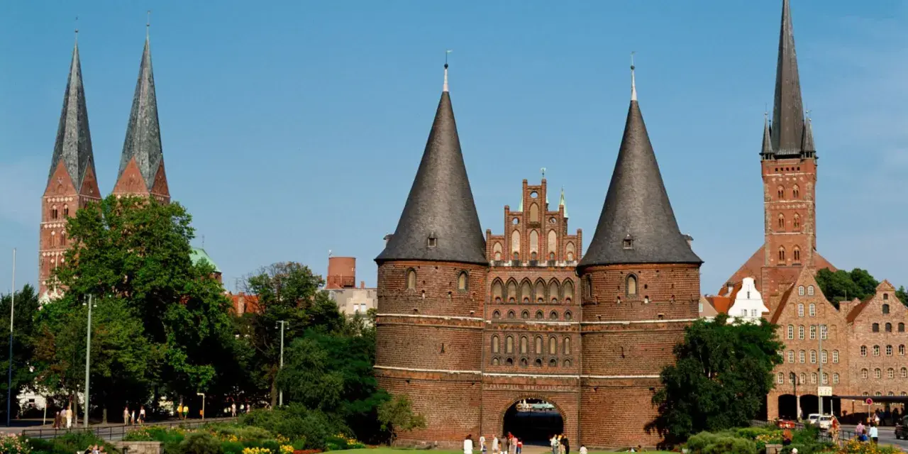 Holstentor in Lübeck, ein Wahrzeichen für Ihre **Ferien Schleswig-Holstein 2025**. Historische Backsteinarchitektur mit Türmen und grünen Parks.