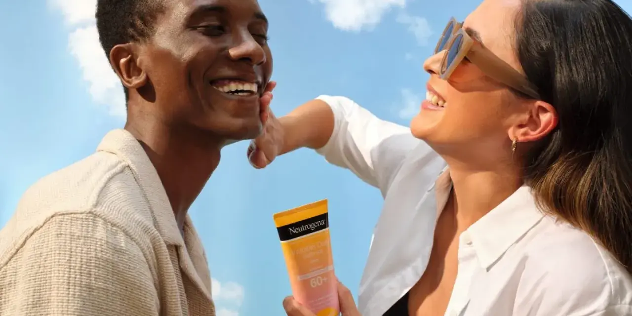 Un couple rit sous un ciel bleu, une femme appliquant une crème solaire Neutrogena. Une liste de protection contre le soleil pour une peau saine.