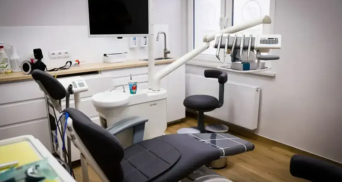 Nowoczesny gabinet stomatologiczny z fotelem, unitem i ekranem.