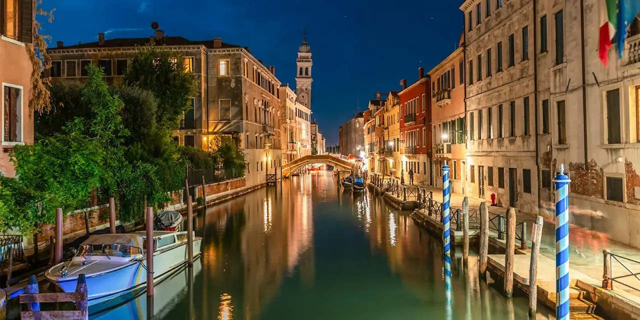 Una gondola venezia di notte, con luci soffuse che si riflettono sull'acqua e un cielo stellato.