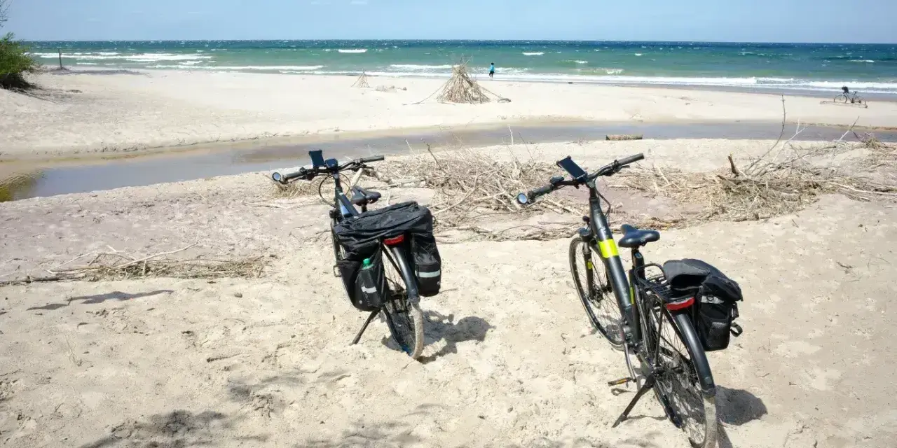 Dwa rowery z sakwami na piaszczystej plaży, gotowe na odkrywanie tras rowerowych nad morzem.