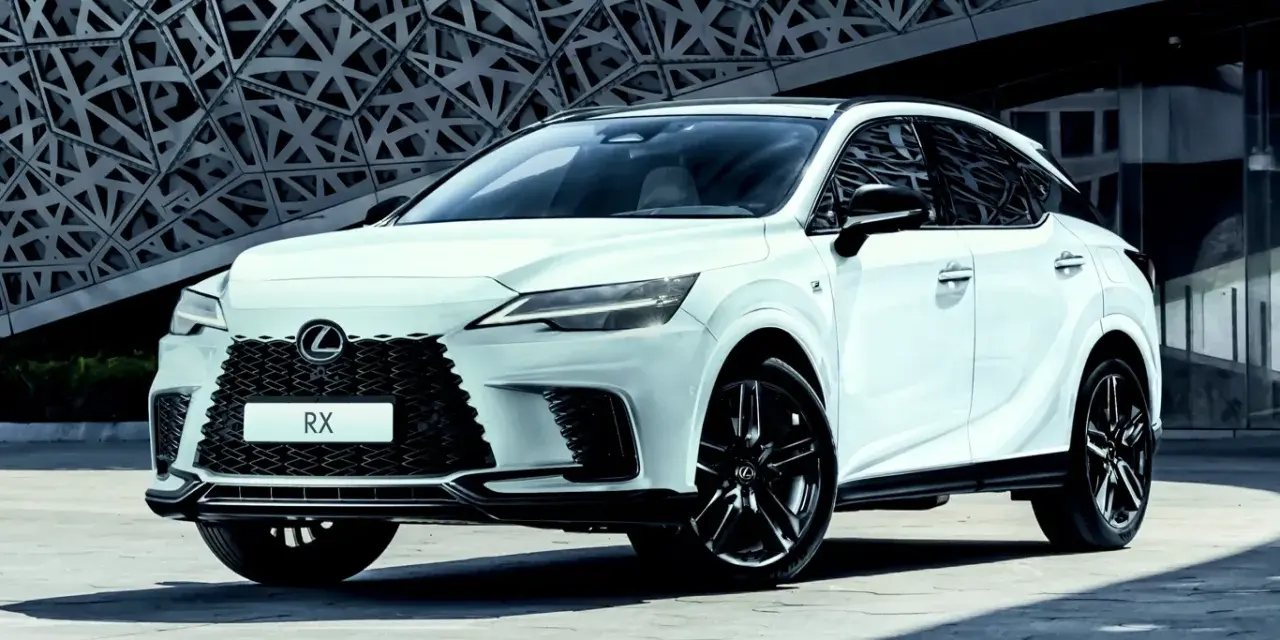 Biały Lexus RX500h z czarnymi felgami stoi przed nowoczesnym budynkiem o geometrycznej fasadzie.