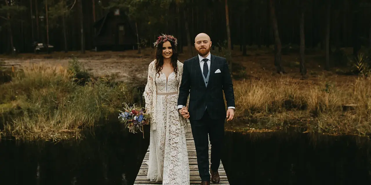 Para idzie przez las, ona w koronkowej sukni i wianku, on w garniturze. Ich suknia ślubna boho rustykalna idealnie pasuje do leśnej scenerii.