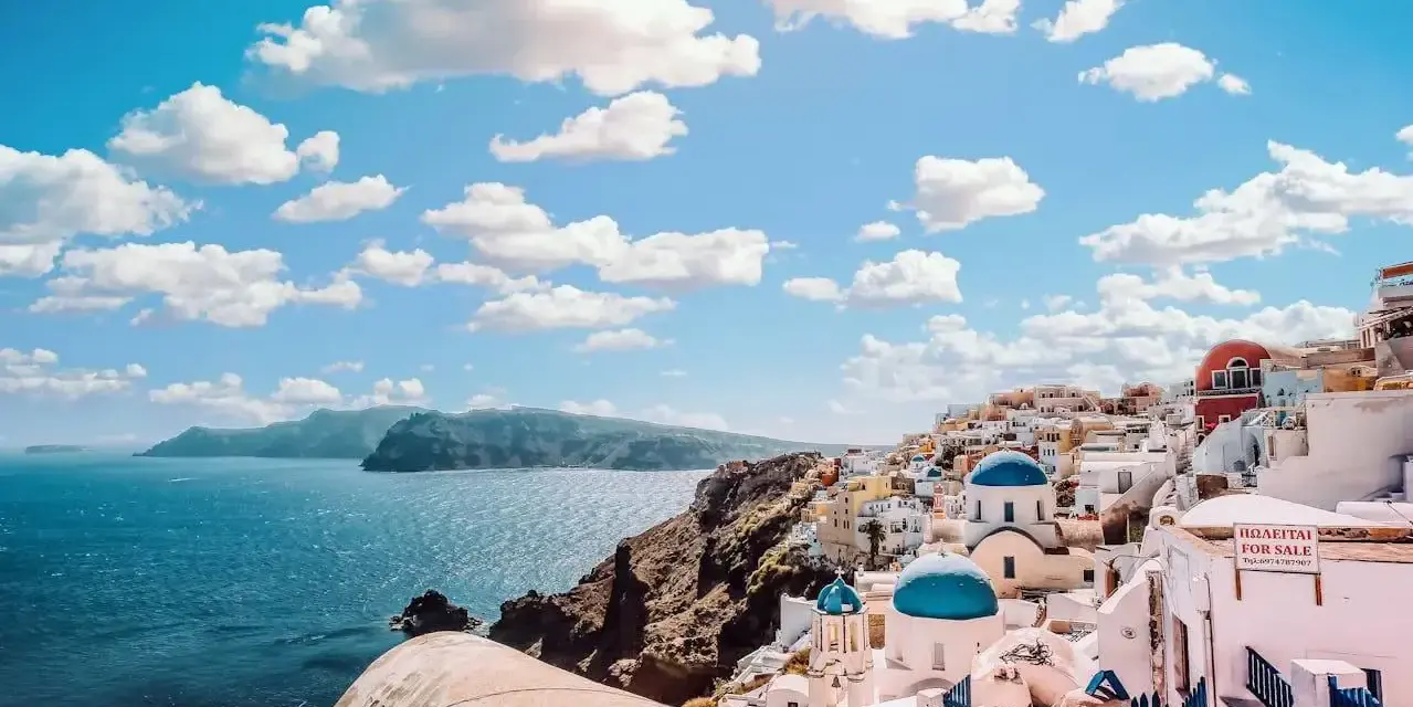 Santorini, Grecja. Ile się leci do raju? Białe domki z niebieskimi kopułami na tle błękitnego morza i nieba.
