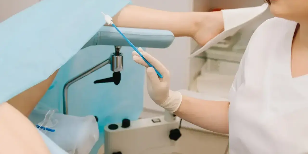 Lekarz przygotowuje się do gbs badanie, trzymając wymazówkę. Pacjentka leży na fotelu ginekologicznym.