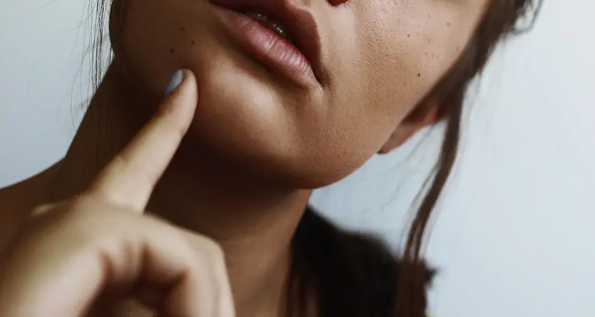 A woman's face, with a finger gently touching her cheek, suggesting a moment of self-care and a relaxing facial massage at home.