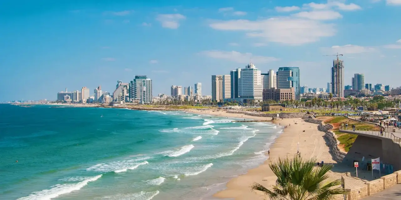 Słoneczna tel aviv plaża z turkusową wodą i nowoczesnymi wieżowcami w tle.