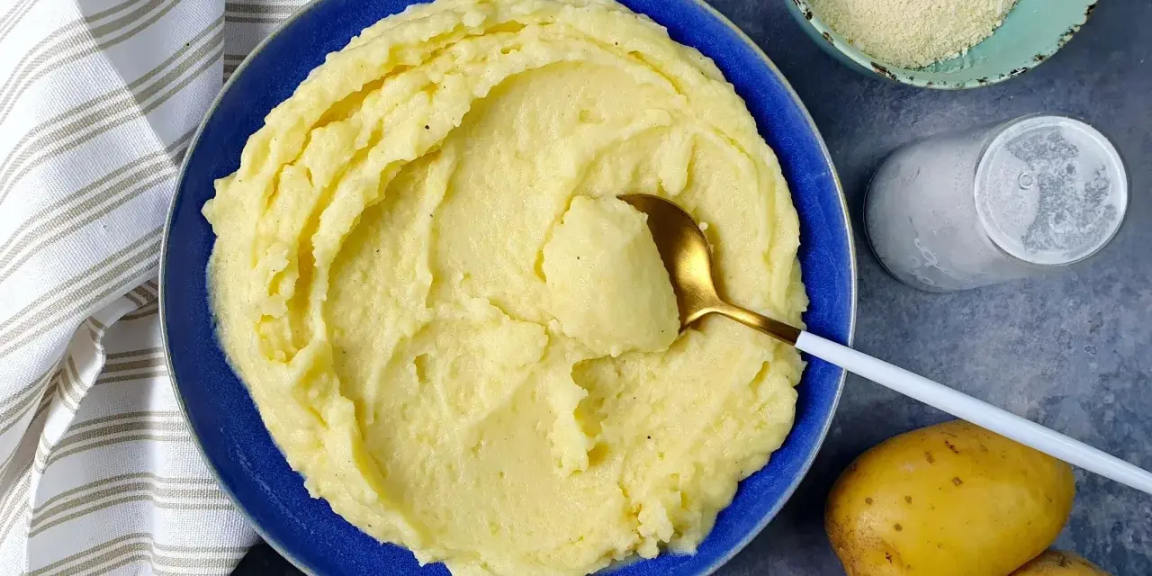 Un piatto di cremoso pure di patate, pronto per essere gustato. Accanto, patate fresche, sale e formaggio grattugiato.