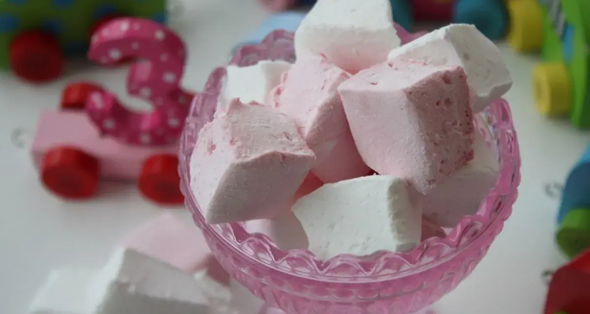 En skål med hemmagjorda marshmallows i rosa och vitt. I bakgrunden syns färgglada träleksaker, som en rosa bil med siffran 3.