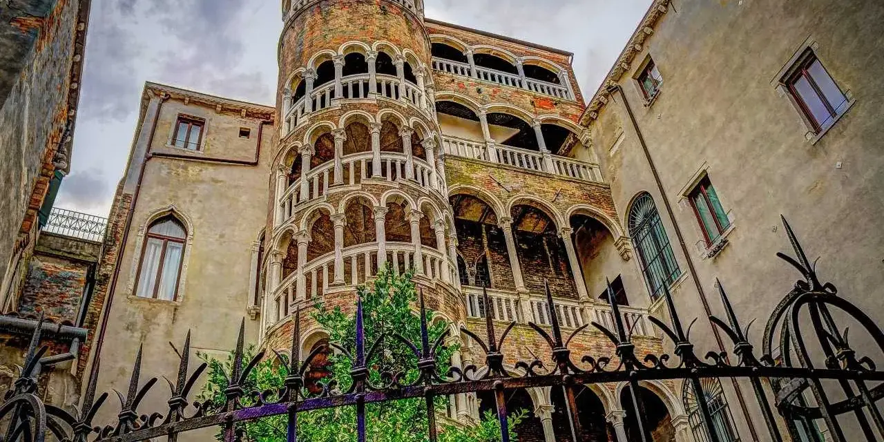 La scala chiocciola di Venezia, con i suoi archi e balconi, si erge maestosa tra antichi palazzi.