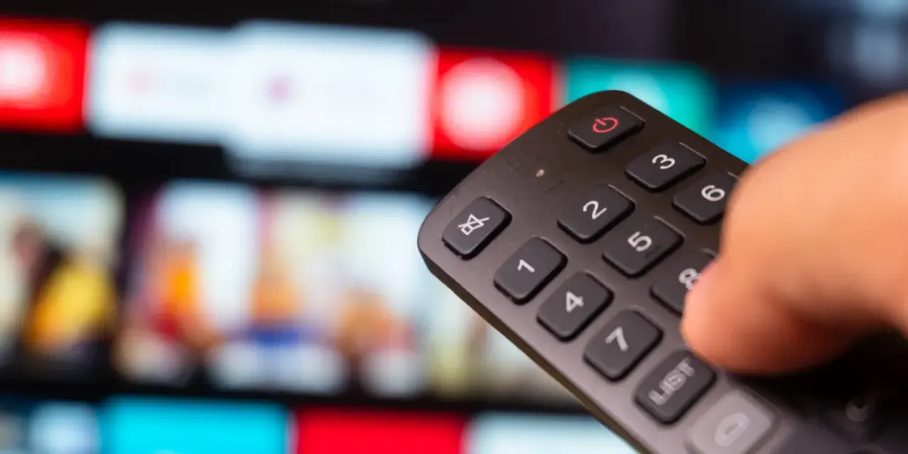 Dłoń trzyma pilot do telewizora, wybierając film na ekranie. To idealny moment na relaks z web tv.