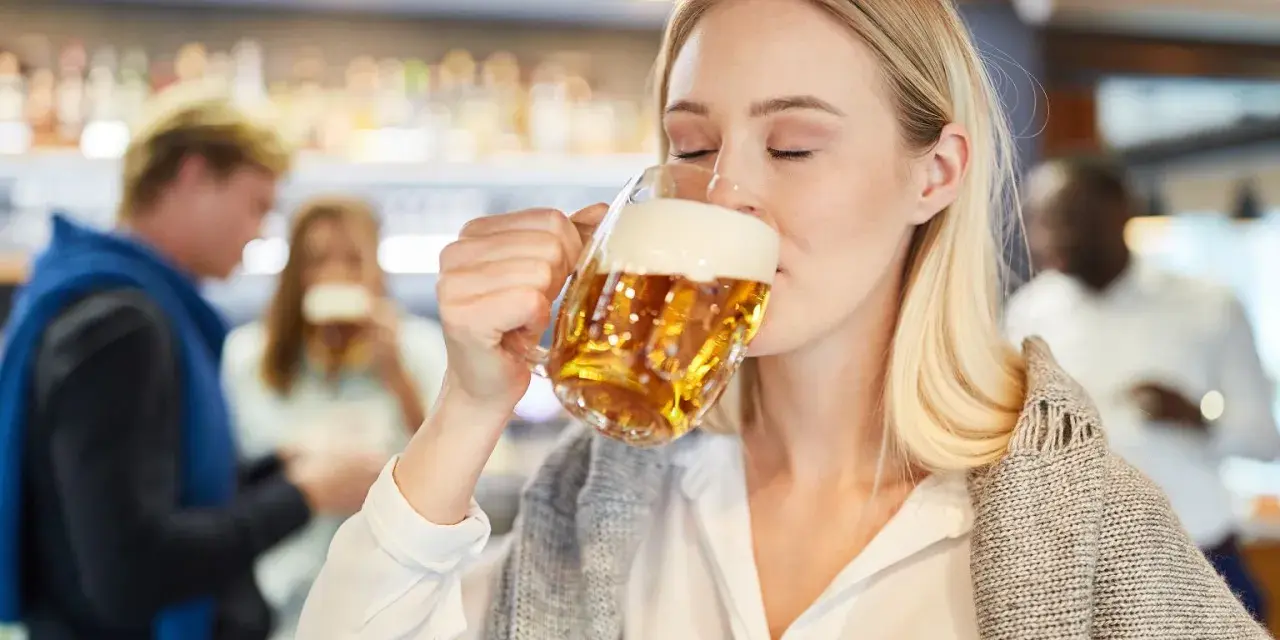 Kobieta z zamkniętymi oczami pije piwo bezalkoholowe w ciąży, ciesząc się smakiem w pubie.