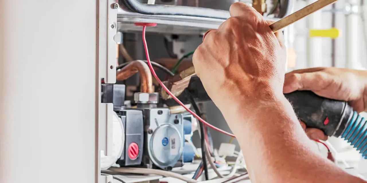 Tecnico che lavora su un **scambiatore acqua calda**, pulendo componenti interni con un pennello e un aspiratore.