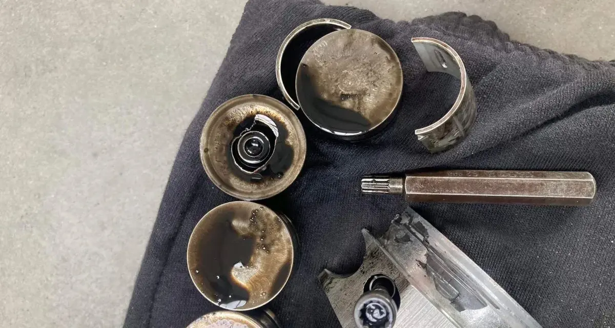 Zużyte popychacze hydrauliczne i inne części silnika pokryte olejem, gotowe do wymiany.