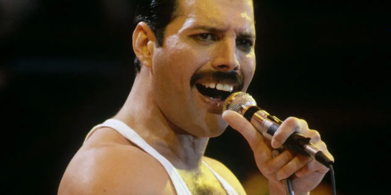 Freddie Mercury śpiewa do mikrofonu, w białej podkoszulce. Wiele osób wspomina go, kiedy zmarł Freddie Mercury.