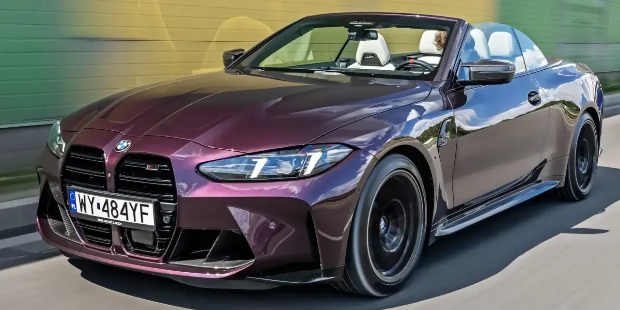 Fioletowe BMW M4 Competition kabriolet pędzi po drodze, odsłaniając białe wnętrze i sportowe detale.