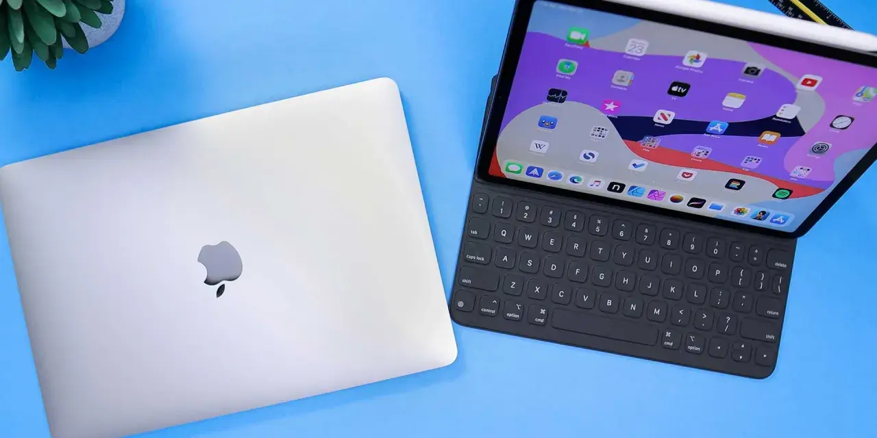 Geschlossenes MacBook neben einem geöffneten iPad Pro mit Tastatur und Apple Pencil.