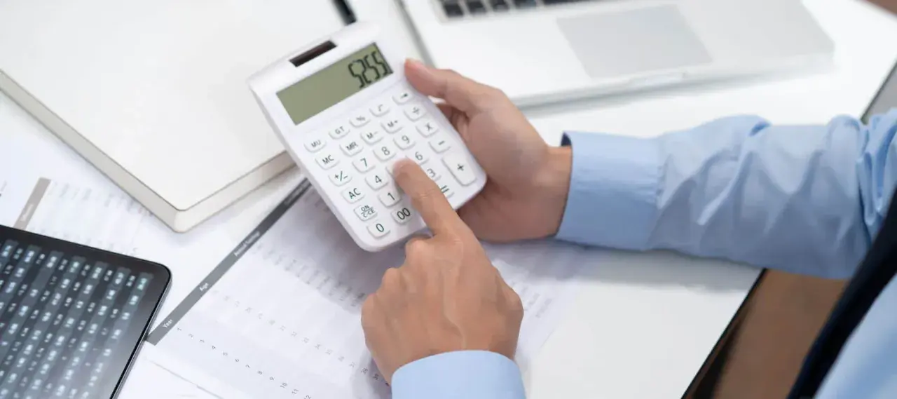 Persona calculando en calculadora blanca, revisando documentos y tablet. Se pregunta cuánto cuesta abrir una empresa en España.