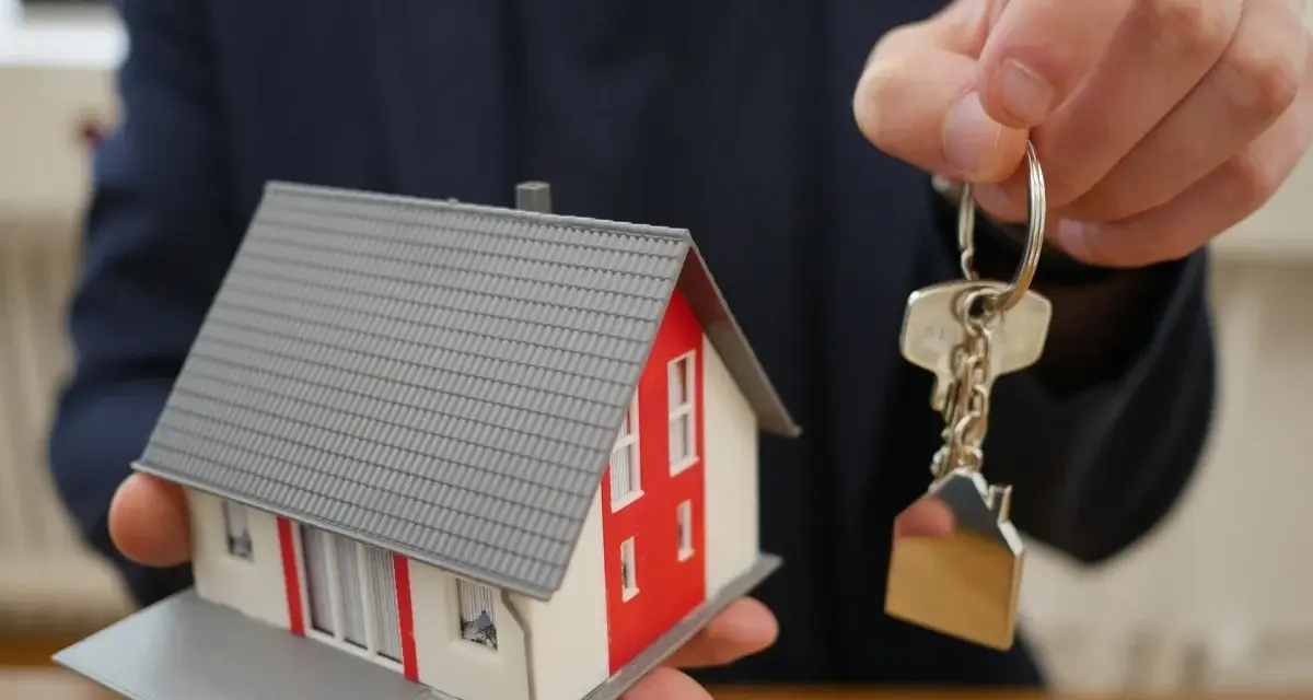 Mano ofrece maqueta de casa y llaves, símbolo de propiedad y seguridad ante la ley antiokupas.