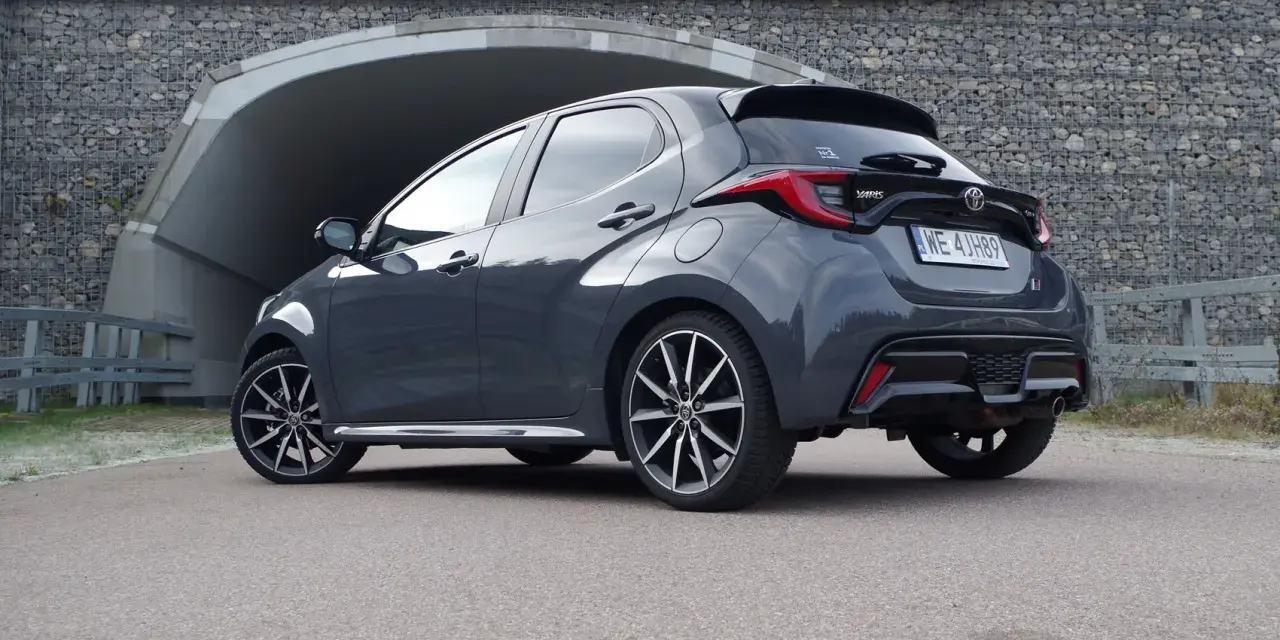 Szary Toyota Yaris GR Sport z czarnym spojlerem i dyfuzorem, zaparkowany przed tunelem.