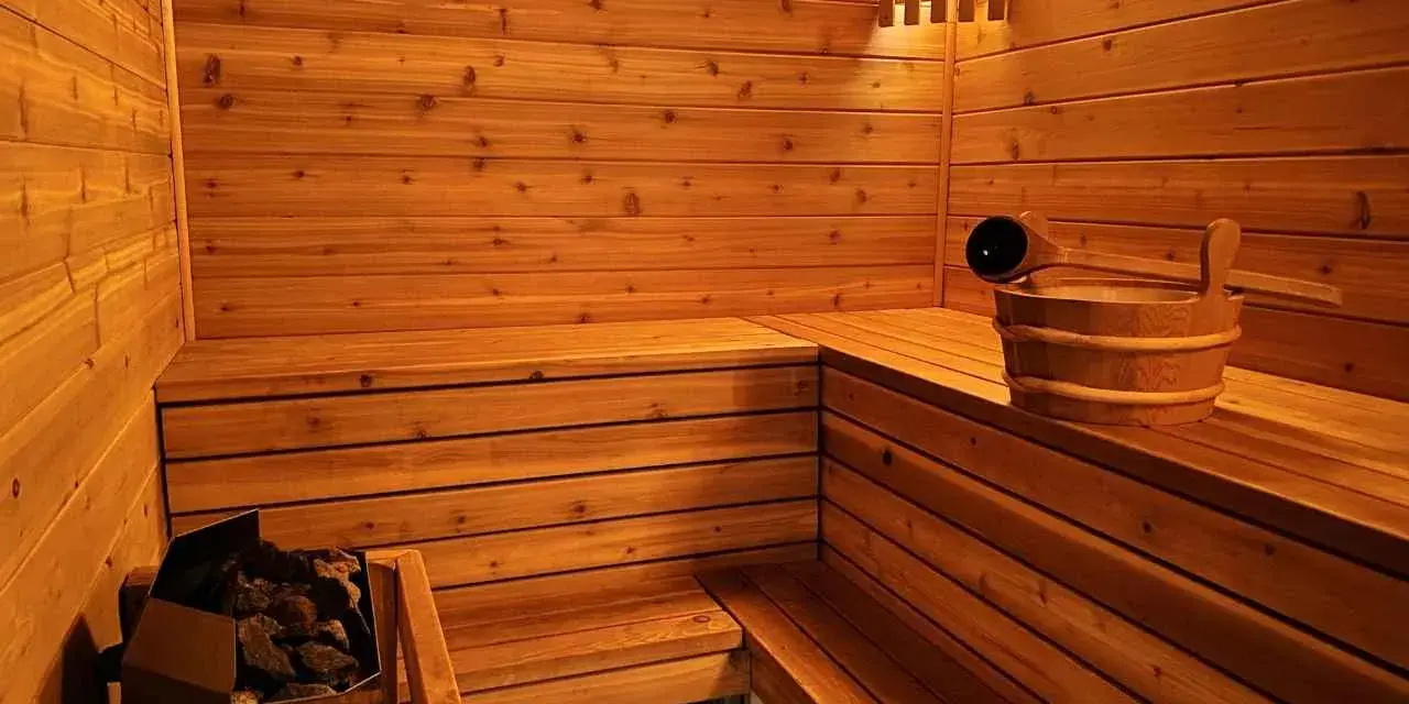 Drewniana sauna z kamieniami i wiadrem. Inspiracja, jak zbudować saunę, by cieszyć się relaksem.