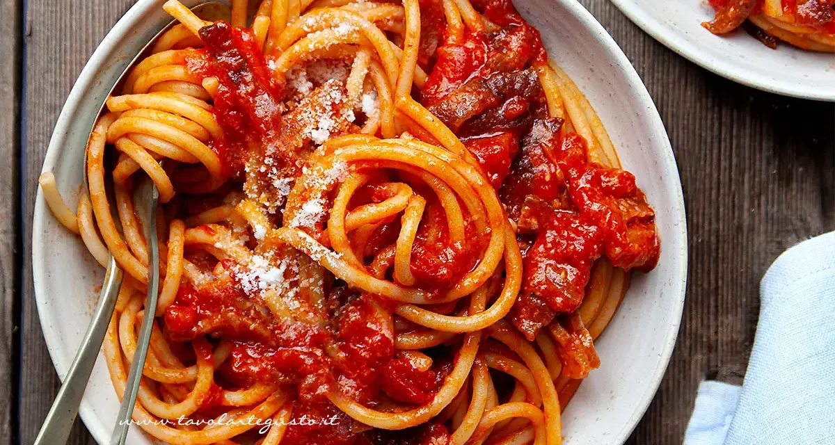 Un piatto fumante di spaghetti conditi con un ricco sugo all'amatriciana ricetta della nonna, cosparso di formaggio grattugiato.