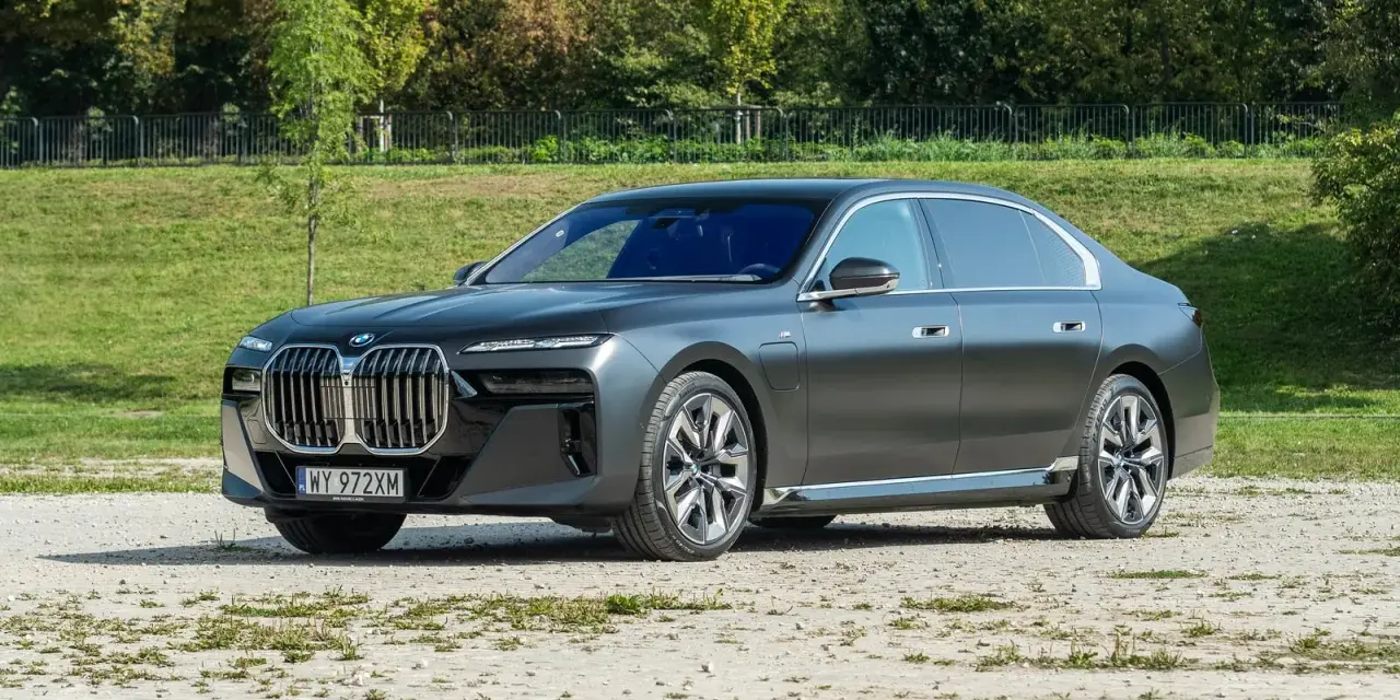 Elegancki, grafitowy BMW 740d na tle zieleni. Luksusowa limuzyna prezentuje się imponująco.