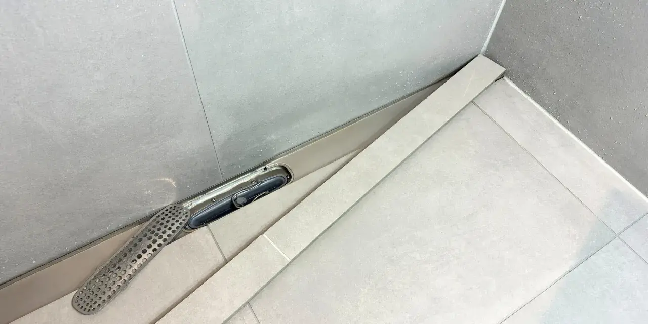 En dusch med en Purus vakuumventil och ett perforerat galler. Vatten droppar på de ljusa kakelplattorna.