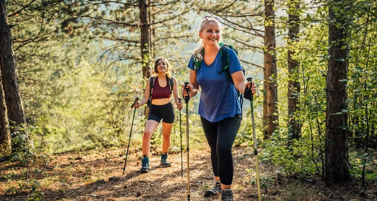 Deux femmes souriantes randonnent en forêt, utilisant des bâtons. Elles semblent apprécier la nature, un argument pour ou contre les bâtons de randonnée.