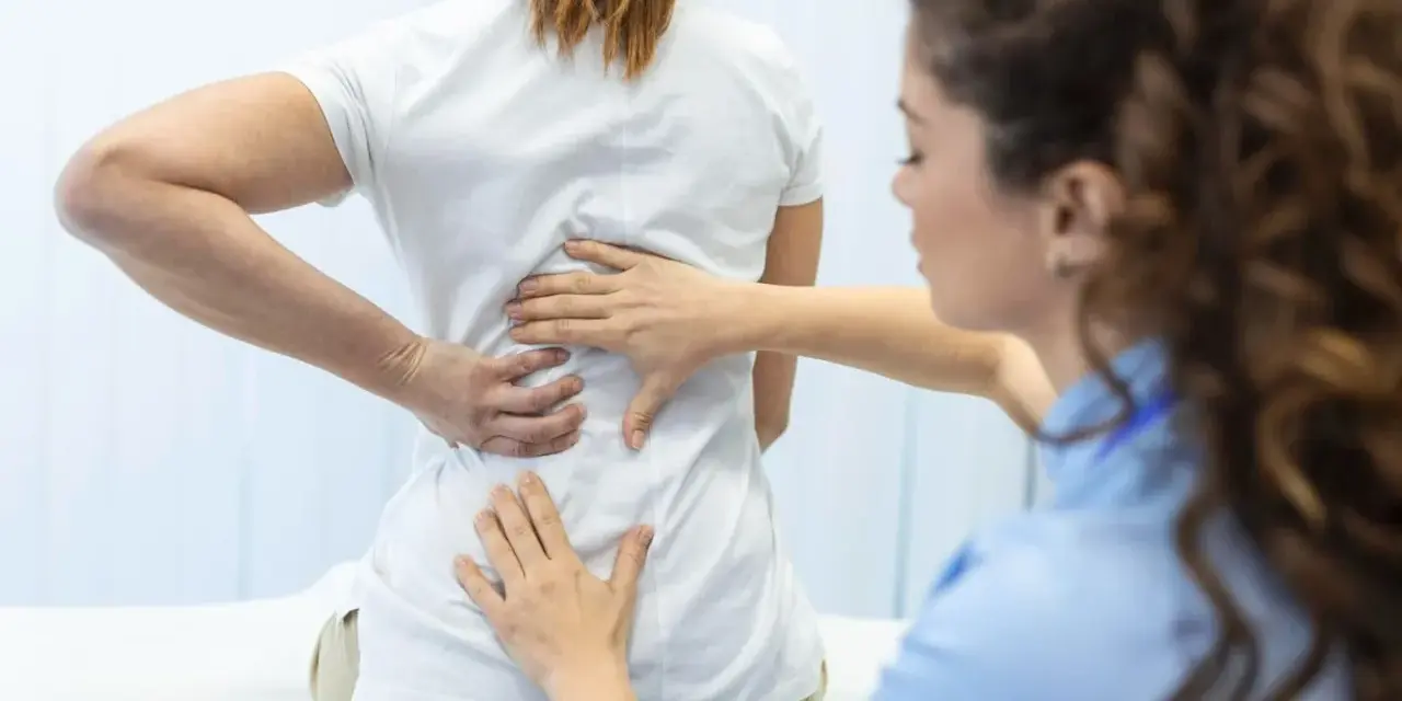 Fizjoterapeuta bada plecy pacjentki. Po długiej rehabilitacji wreszcie wyleczyłem kręgozmyk i czuję się znacznie lepiej.