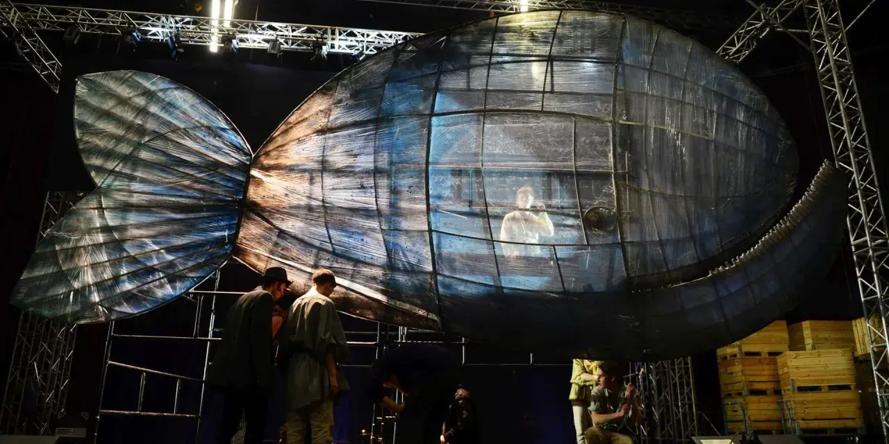 Scena teatralna z wielką, szklaną rybą, w której siedzi człowiek. To może być cud Jonasza.