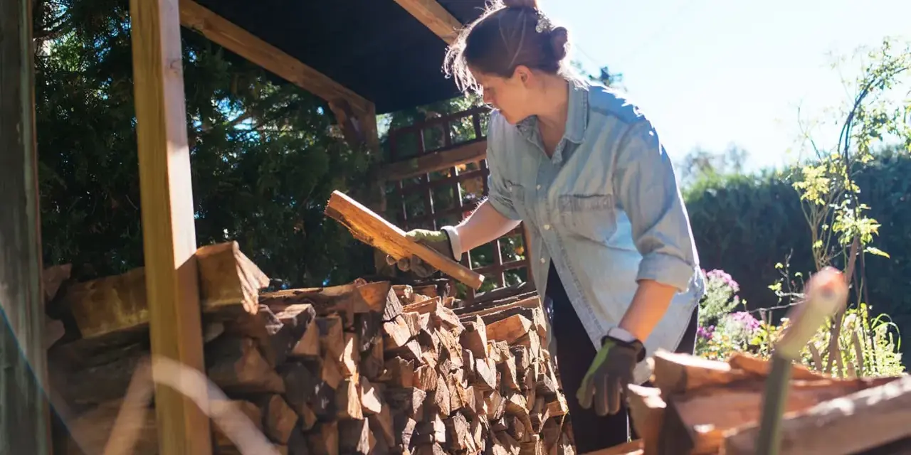 Femme avec des bûches de bois sous un abri.