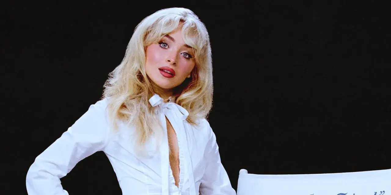 Sabrina Carpenter w białej koszuli, z rozpuszczonymi blond włosami, wygląda jak "man's best friend" na tle czerni.