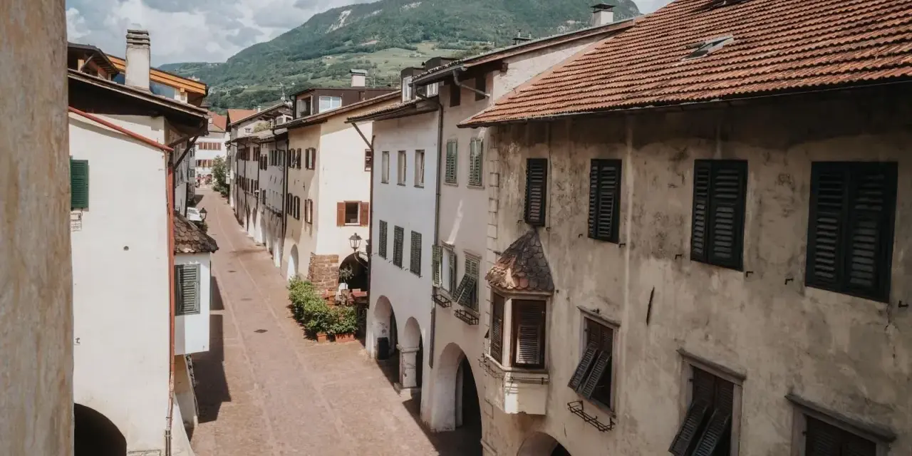 Antica via del vino con case color crema, persiane verdi e un monte sullo sfondo.